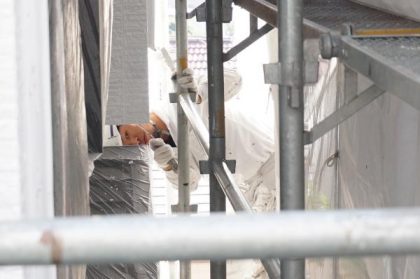 足場越しに見える塗装作業中の外壁塗装専門店功栄の職人